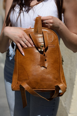 girl in white leggings and T-shirt with a light brown leather backpack in her handsの写真素材