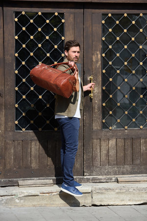 a man with a bag. black leather travel bag, street photo. man is wearing blue sneakers, jeans, a white T-shirt and a jacketの写真素材