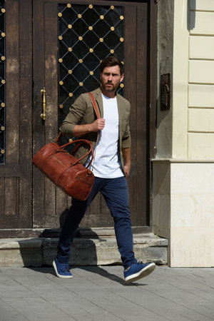 a man with a bag. black leather travel bag, street photo. man is wearing blue sneakers, jeans, a white T-shirt and a jacketの写真素材