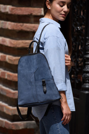 Beautiful young girl wearing blue jeans, shirt and white t-shirt posing with blue leather backpackの写真素材