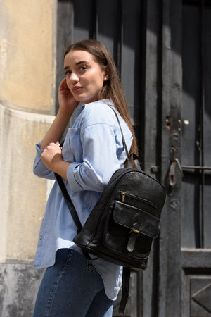 Beautiful young girl wearing blue jeans, shirt and white t-shirt posing with black leather backpackの写真素材
