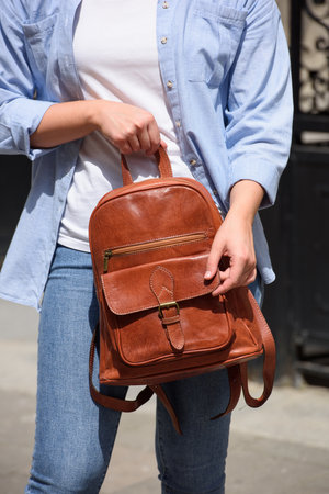 Beautiful young girl wearing blue jeans, shirt and white t-shirt posing with brown leather backpackの写真素材