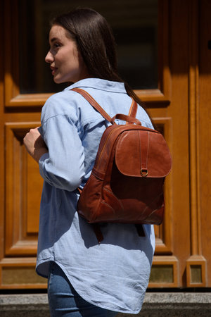 Beautiful young girl wearing blue jeans, shirt and white t-shirt posing with brown leather backpackの写真素材