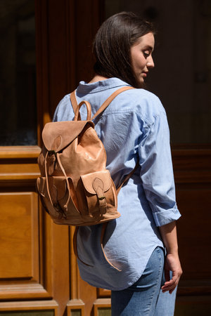 Beautiful young girl wearing blue jeans, shirt and white t-shirt posing with beige leather backpackの写真素材