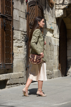 pretty brunette girl in satin long dress ankle strap shoes and checkered jacket posing with leather handbagの写真素材