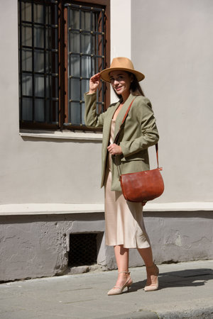 pretty brunette girl in satin long dress ankle strap shoes and checkered jacket posing with leather handbagの写真素材