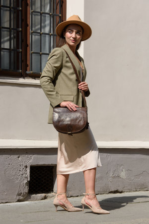 pretty brunette girl in satin long dress ankle strap shoes and checkered jacket posing with leather handbagの写真素材