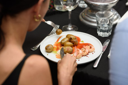 women eating traditional spanish tapas served on plates on black table background. Patatas Bravas with Gambas Ajilloの写真素材
