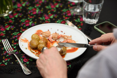 man eating traditional spanish tapas served on plates on black table background. Patatas Bravas with Gambas Ajilloの写真素材