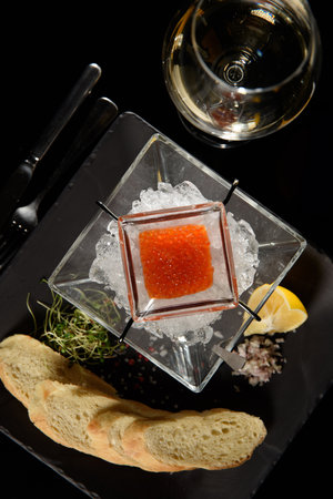 salmon fish caviar, on ice, with croutons, lemon, on a transparent dish, on a dark backgroundの写真素材