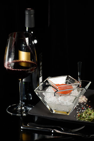 salmon fish caviar, on ice, with croutons, lemon, on a transparent dish, on a dark backgroundの写真素材