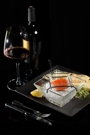 salmon fish caviar, on ice, with croutons, lemon, on a transparent dish, on a dark backgroundの写真素材