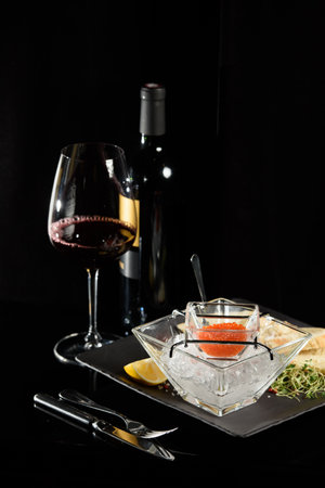 salmon fish caviar, on ice, with croutons, lemon, on a transparent dish, on a dark backgroundの写真素材