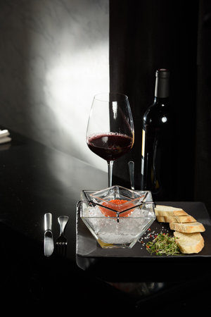salmon fish caviar, on ice, with croutons, lemon, on a transparent dish, on a dark backgroundの写真素材
