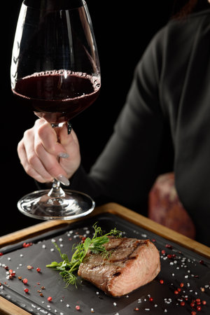 Woman sitting at a table in a restaurant. He is holding a glass of red wine and eating a steakの写真素材