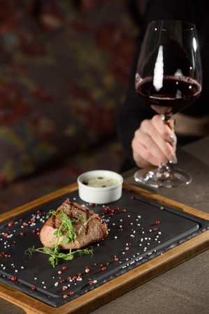 Woman sitting at a table in a restaurant. He is holding a glass of red wine and eating a steakの写真素材