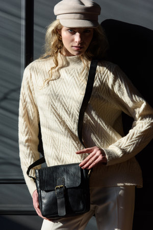 Studio portrait of beautiful woman with a curly blond hair holding black bag, posing on gray background.の写真素材
