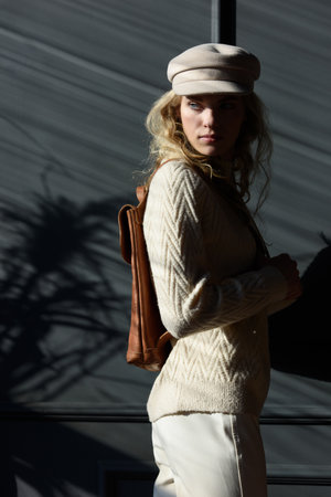 Studio portrait of beautiful woman with a curly blond hair holding brown backpack, posing on gray background.の写真素材