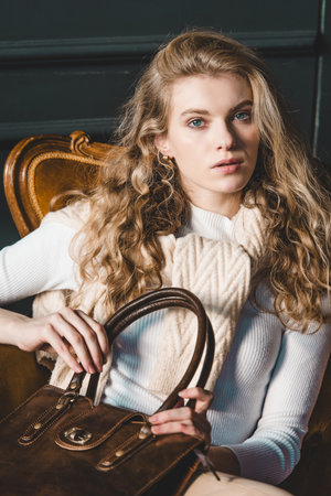 beautiful curly blond hair woman posing with a small shopper brown bag in a vintage chairの写真素材