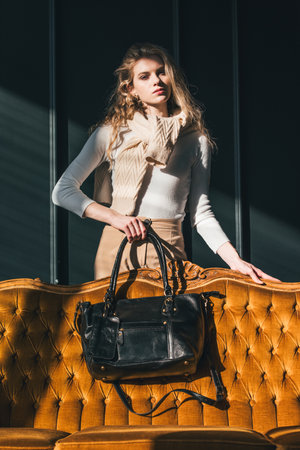 beautiful curly blond hair woman posing with a small black shopper bag near vintage volor sofaの写真素材