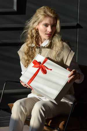 A woman in a chair holds a white gift box with a red ribbonの写真素材