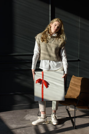 A woman holds a white gift box with a red ribbonの写真素材
