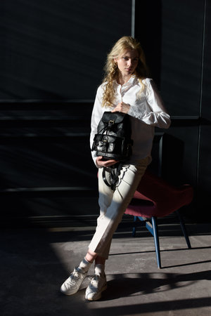 beautiful curly blond hair woman posing with a black leather backpackの写真素材