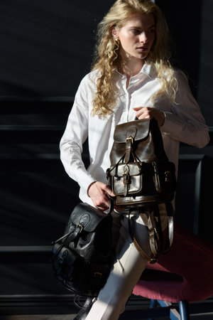 beautiful curly blond hair woman posing with a two leather backpacksの写真素材