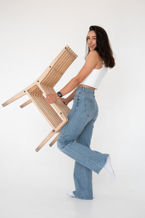 Happy beautiful girl posing with a chair in a new hot look. Wearing blue jeans and white waistcoatの写真素材