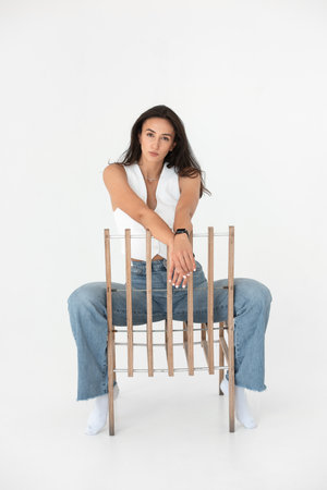 Happy beautiful girl posing with a chair in a new hot look. Wearing blue jeans and white waistcoatの写真素材