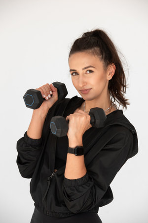 Young girl posing with dumbbells for power training, indoors. athlete wearing black leggings and shirtの写真素材