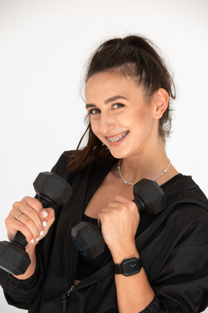 Young girl posing with dumbbells for power training, indoors. athlete wearing black leggings and shirtの写真素材