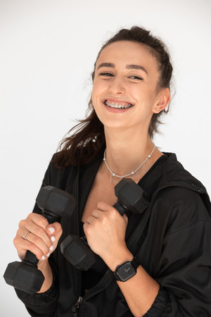 Young girl posing with dumbbells for power training, indoors. athlete wearing black leggings and shirtの写真素材
