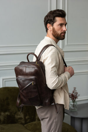 A Stylish and Professional Man Standing with a brown backpack in a Contemporary Modern Setting.の写真素材