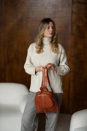 girl in gray pants and beige sweater posing with a small shiny brown leather backpackの写真素材
