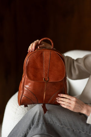 a woman in gray pants and beige sweater posing with a brown leather backpackの写真素材