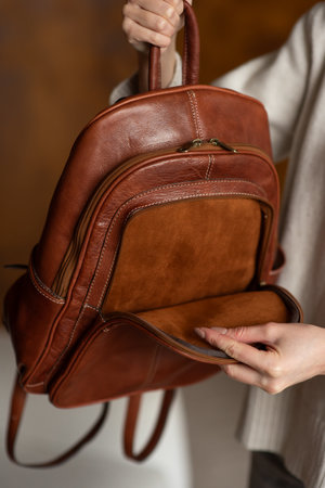 beautiful girl in gray pants and beige sweater posing with a small shiny brown leather backpackの写真素材