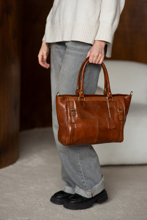 beautiful girl in gray pants and beige sweater posing with a small shiny brown leather bagの写真素材