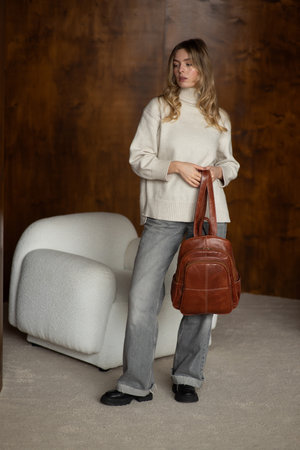 beautiful girl in gray pants and beige sweater posing with a small shiny brown leather backpackの写真素材