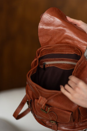 beautiful girl in gray pants and beige sweater posing with a small shiny brown leather backpackの写真素材