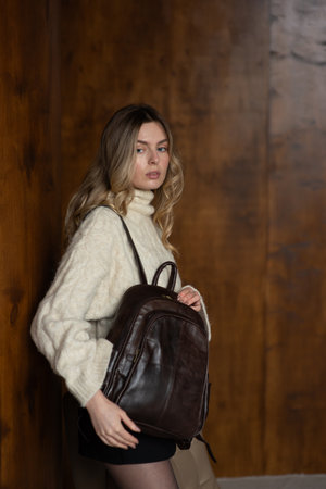 A girl in a warm sweater, a black short skirt, nylon tights, and black shoes is posing with a brown backpack.の写真素材