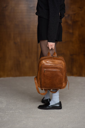 A girl in a warm sweater, a black short skirt, nylon tights, and black shoes is posing with a brown backpack.の写真素材