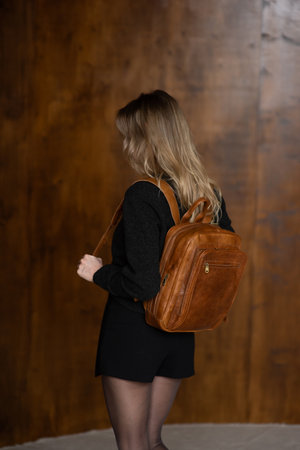 A girl in a warm sweater, a black short skirt and nylon tights is posing with a brown backpack.の写真素材