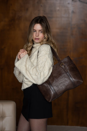 A girl in a warm sweater, a black short skirt, nylon tights is posing with a brown leather bag.の写真素材
