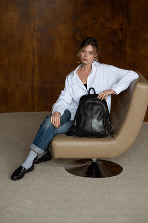 A girl in a white shirt blue jeans and loafers is posing with a black backpack.の写真素材