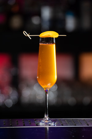 A vibrant orange cocktail is served in a tall, slender glass, garnished with a thin slice of orange peel skewered across the rim.の写真素材