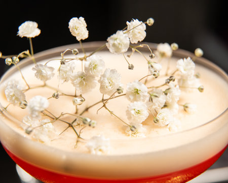 blush-toned cocktail with a frothy top is elegantly garnished with delicate white babys breath flowers, presented on a golden tray alongside a vintage-style perfume atomizerの写真素材