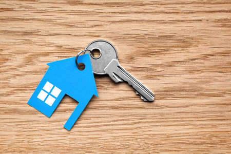 Silver key with blue house figure on wooden background