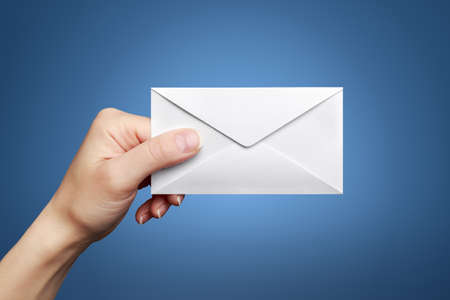 Woman's hand holding closed envelope against blue backgroundの写真素材