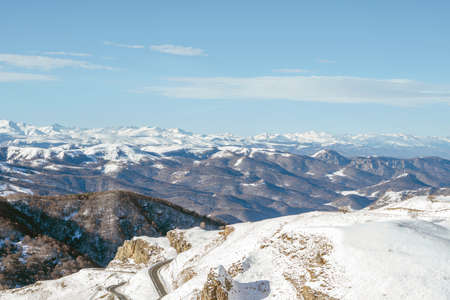 View of the snow-covered mountain range of the Caucasus Mountains and the pine forest from the pass. Clear day and blue skyの写真素材